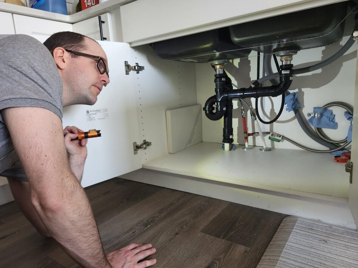 Plumbing and Drainage Inspection by a Licensed Home Inspector | At Ease Property Inspections Erich Kamprath inspecting under-sink plumbing connections and drainage as part of a detailed residential home inspection in the North Okanagan