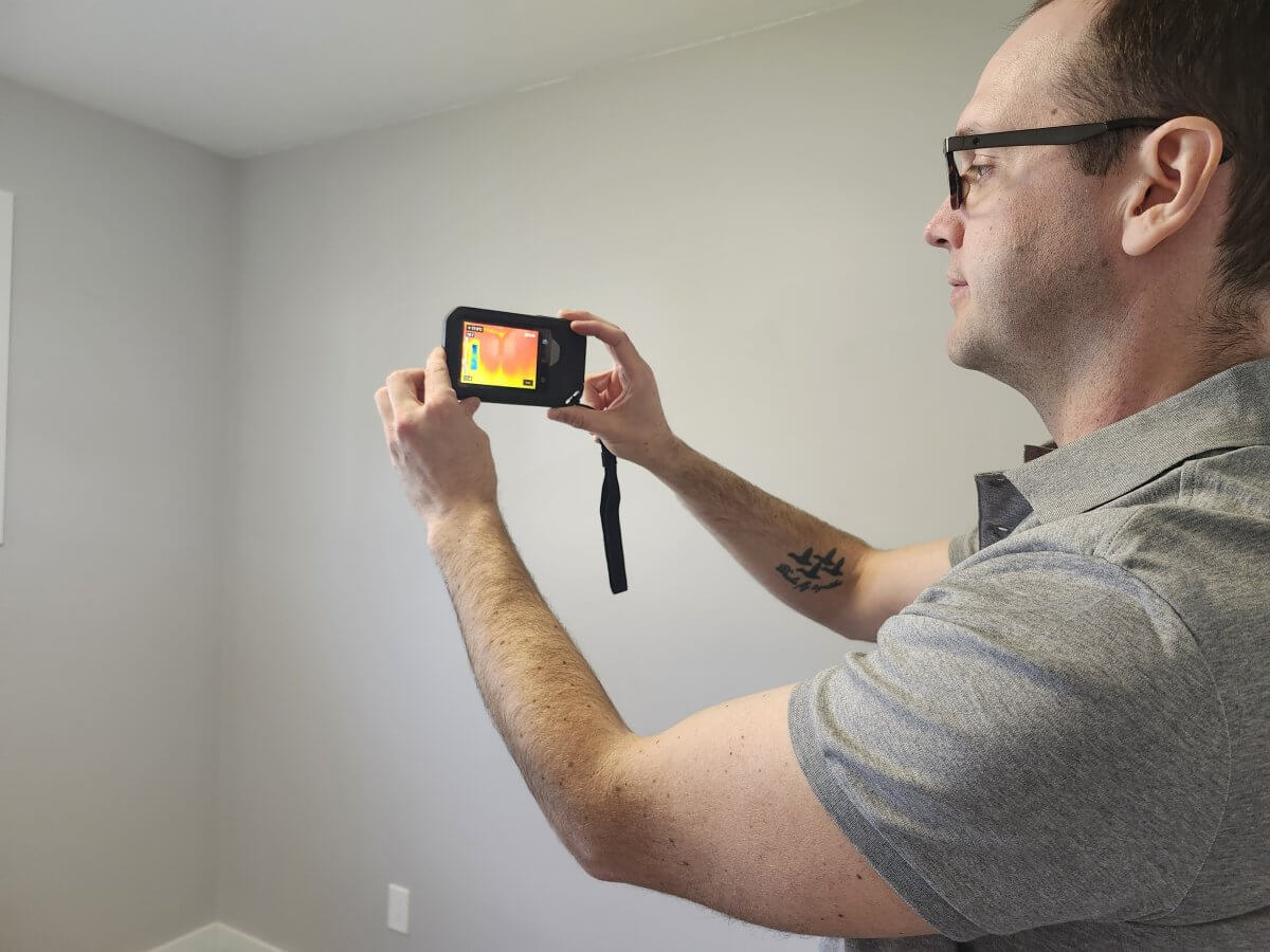 Infrared Thermal Imaging Used in Professional Home Inspections | At Ease Property Inspections Home inspector using an infrared thermal imaging camera to identify heat loss and potential insulation issues inside a residential property