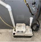 A close-up of a condensate pump system connected to a furnace or HVAC unit, with PVC piping and electrical wiring visible. This component helps remove excess moisture to prevent leaks and water damage. At Ease Property Inspections, serving Vernon and the Okanagan, carefully inspects mechanical systems to ensure homes remain safe, efficient, and water-tight.